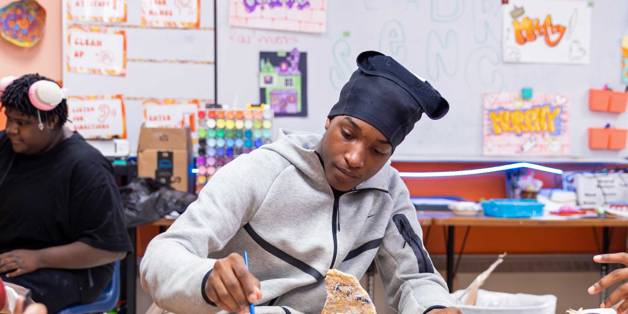 Student painting a project at a table in an art classroom.