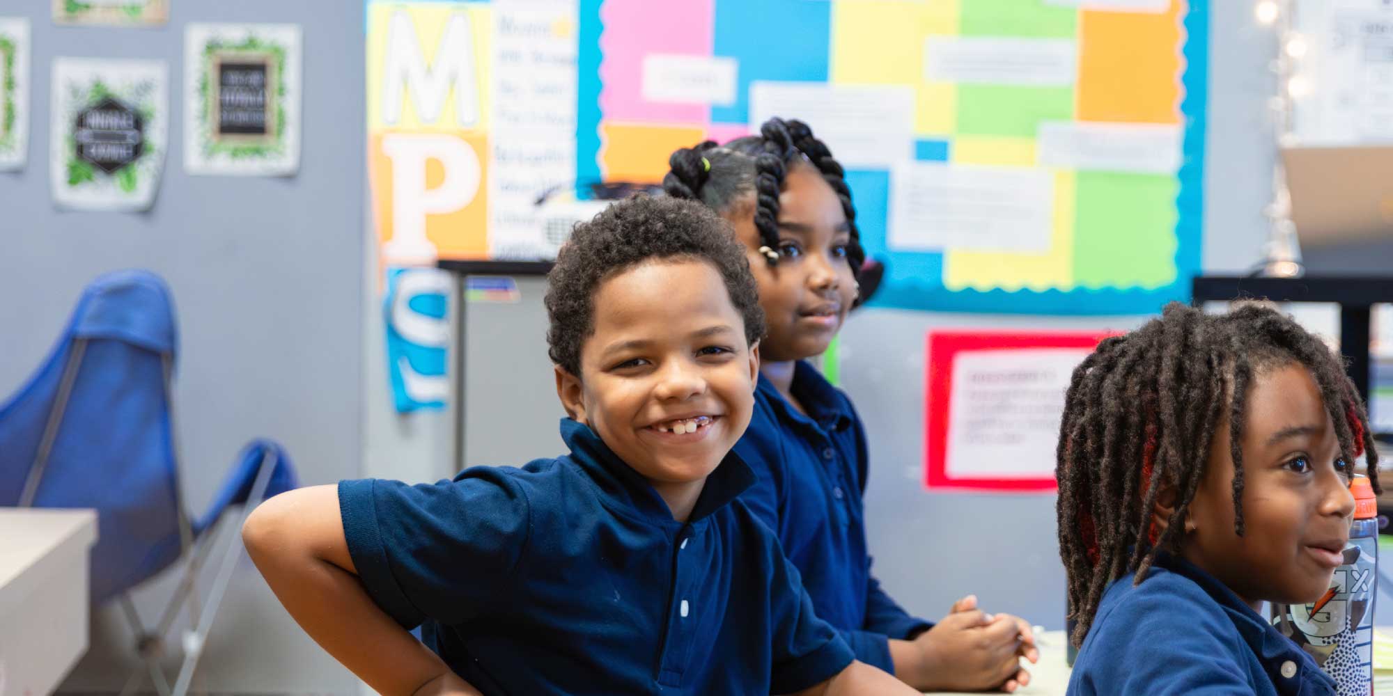 Smiling students in navy uniforms sitting together in a classroom.