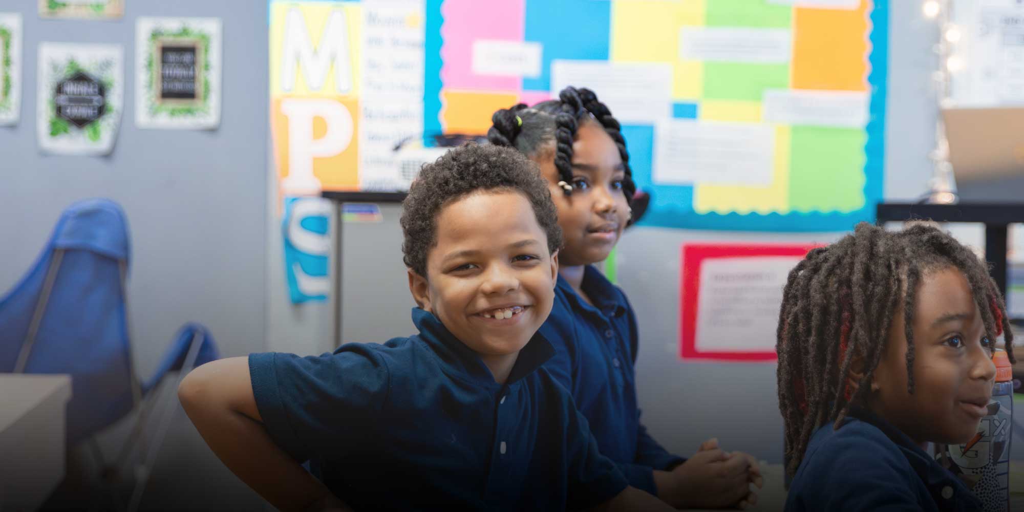 Smiling students in navy uniforms sitting together in a classroom.