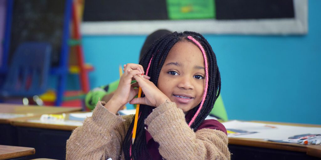Student smiling whiles holding a pencil in class